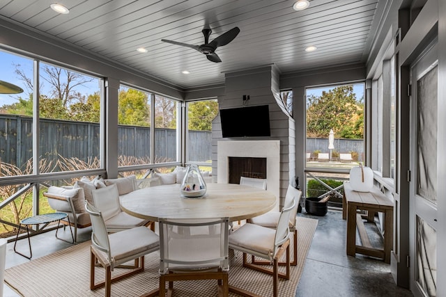 sunroom with a healthy amount of sunlight, a large fireplace, wooden ceiling, and a ceiling fan