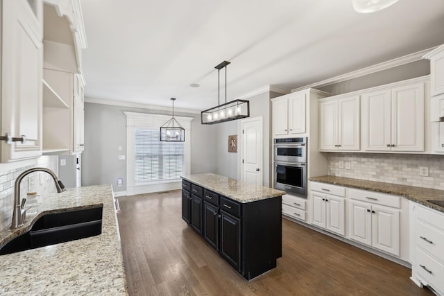 kitchen with double oven, dark cabinetry, a sink, and white cabinetry