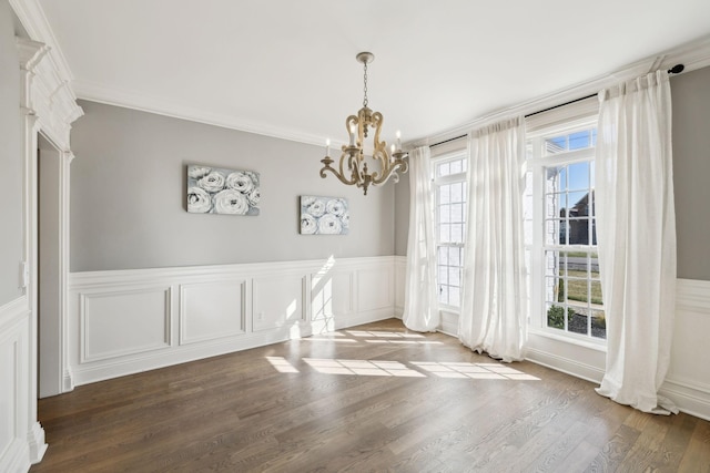 unfurnished dining area with a notable chandelier, crown molding, wood finished floors, and wainscoting