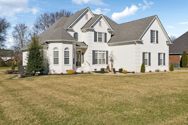 view of front of house with cooling unit, brick siding, a front lawn, and roof with shingles