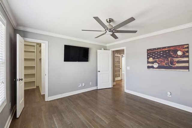 unfurnished bedroom featuring baseboards, a spacious closet, dark wood-style flooring, and crown molding