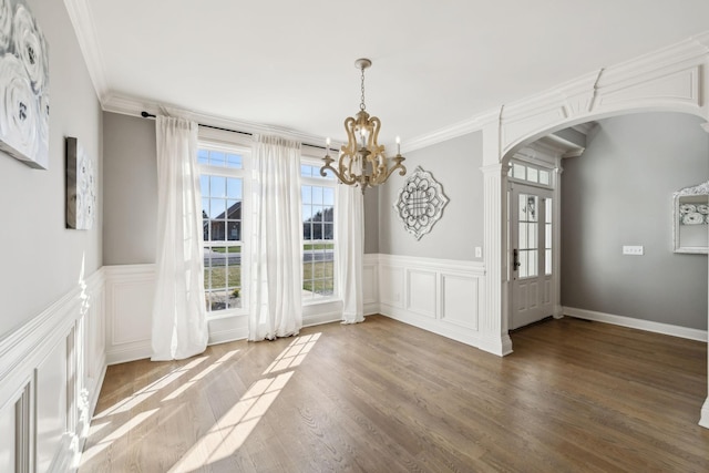 unfurnished dining area with arched walkways, an inviting chandelier, ornamental molding, wainscoting, and wood finished floors