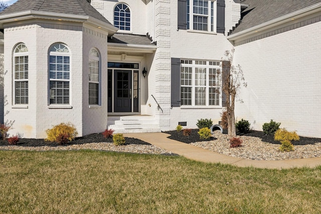 property entrance with crawl space, a shingled roof, a lawn, and brick siding