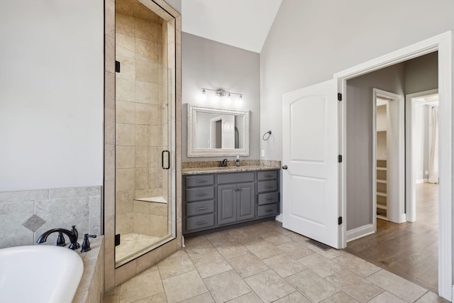 full bath with a stall shower, tiled bath, lofted ceiling, tile patterned floors, and vanity