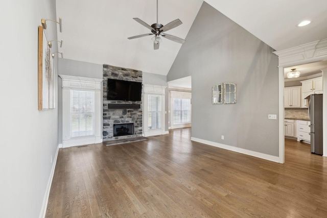 unfurnished living room with plenty of natural light, baseboards, wood finished floors, and a stone fireplace