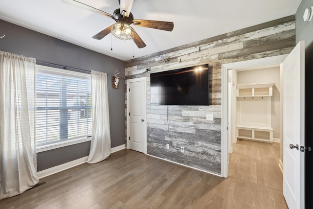 unfurnished living room featuring baseboards, a ceiling fan, an accent wall, wood finished floors, and wood walls