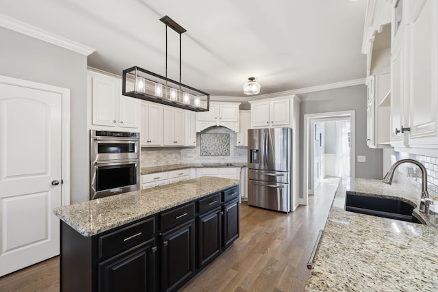 kitchen featuring appliances with stainless steel finishes, ornamental molding, white cabinetry, a sink, and dark cabinets