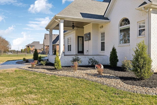 view of side of home with brick siding, a yard, roof with shingles, a ceiling fan, and fence