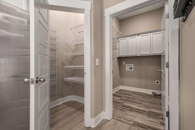 laundry room featuring hookup for a washing machine, wood finished floors, baseboards, cabinet space, and electric dryer hookup