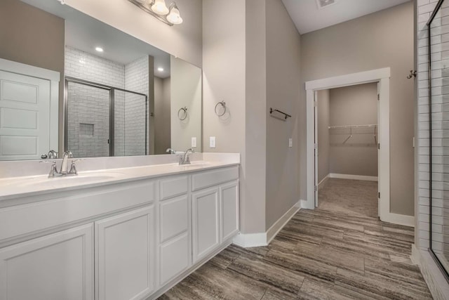 full bathroom featuring wood finished floors, a sink, baseboards, a stall shower, and a walk in closet