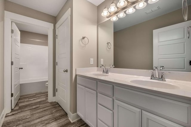 bathroom with double vanity, visible vents, a sink, and wood finished floors