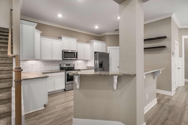 kitchen with tasteful backsplash, light wood-style flooring, appliances with stainless steel finishes, white cabinetry, and light stone countertops