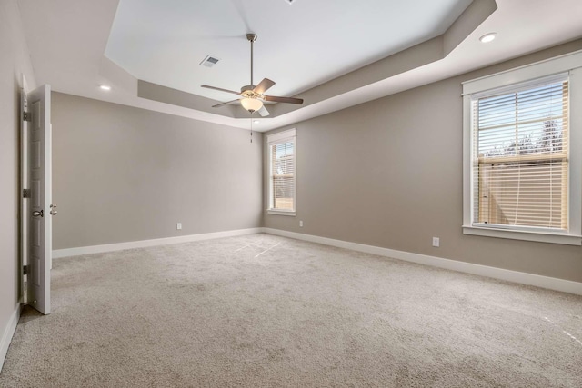 carpeted empty room featuring a ceiling fan, a raised ceiling, a healthy amount of sunlight, and baseboards