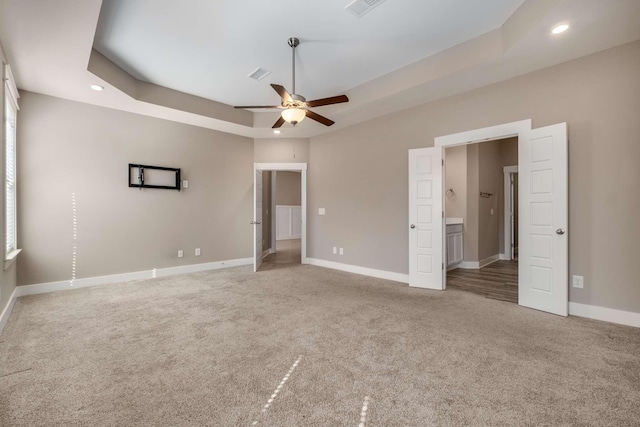 unfurnished bedroom with a tray ceiling, light carpet, and baseboards