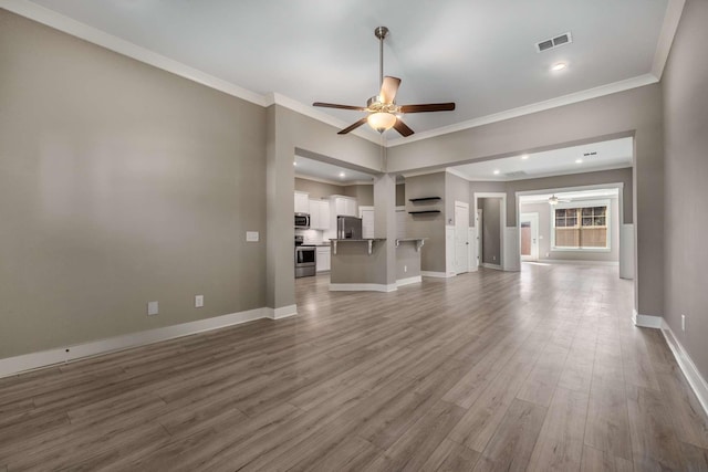 unfurnished living room with baseboards, visible vents, ceiling fan, ornamental molding, and wood finished floors