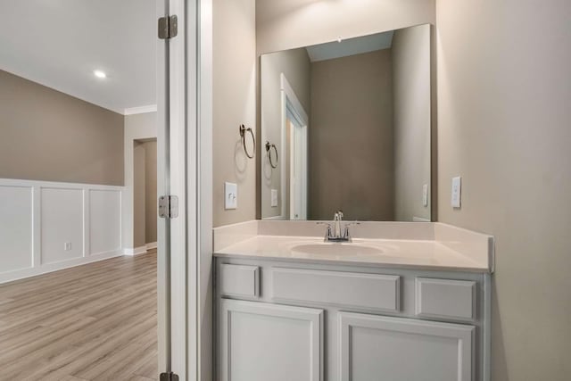 bathroom with vanity, a decorative wall, wood finished floors, and wainscoting