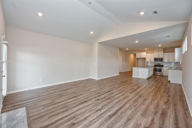 unfurnished living room featuring baseboards, visible vents, lofted ceiling, light wood-type flooring, and a sink