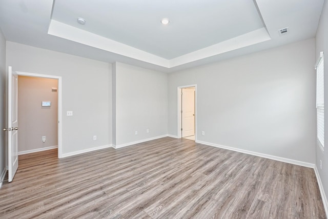 empty room with baseboards, visible vents, a tray ceiling, and wood finished floors