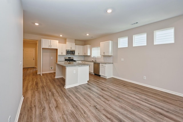 kitchen with stainless steel appliances, decorative backsplash, white cabinets, a sink, and light wood-type flooring