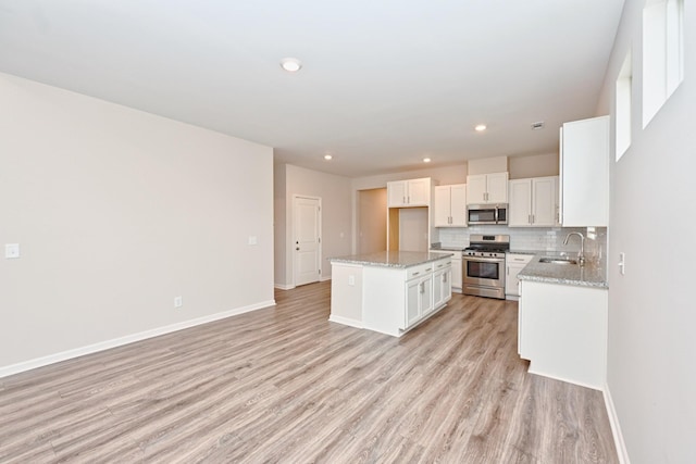 kitchen with stainless steel appliances, backsplash, light wood-type flooring, and a sink