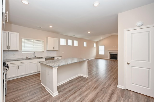 kitchen featuring tasteful backsplash, white cabinetry, a kitchen island, a sink, and light wood-type flooring