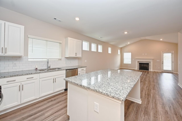 kitchen with white cabinets, lofted ceiling, light wood-style flooring, a kitchen island, and a sink