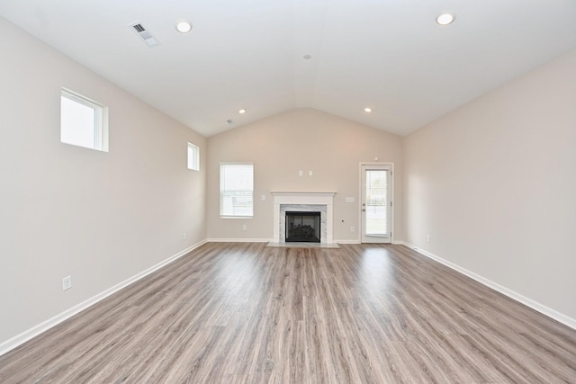 unfurnished living room featuring a premium fireplace, wood finished floors, visible vents, baseboards, and vaulted ceiling