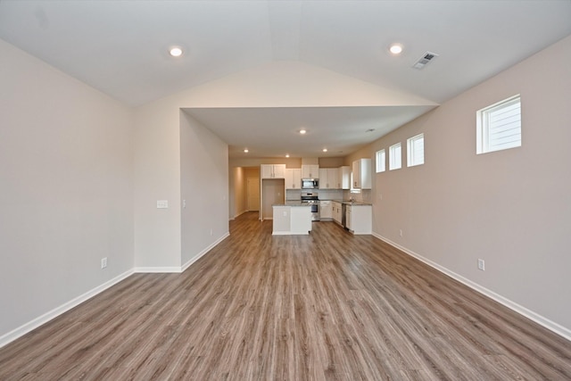 unfurnished living room with baseboards, visible vents, vaulted ceiling, and wood finished floors