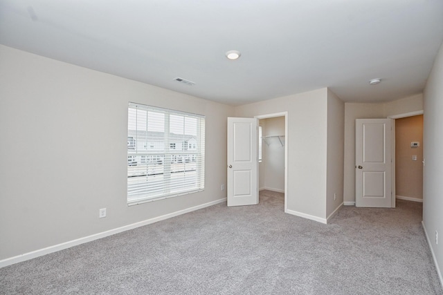 unfurnished bedroom with carpet floors, a walk in closet, a closet, visible vents, and baseboards