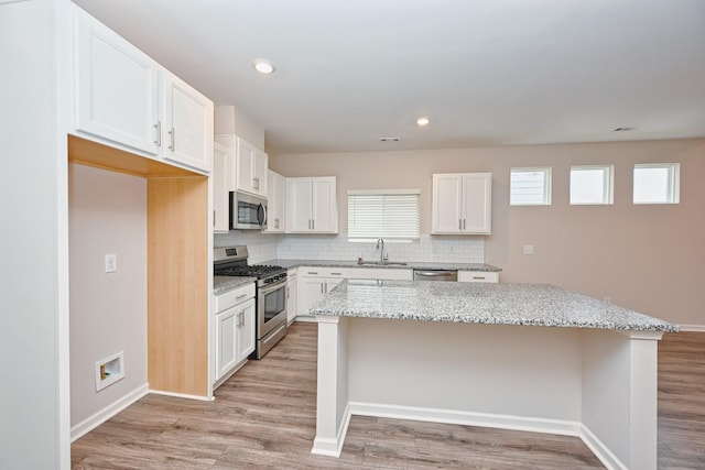 kitchen featuring stainless steel appliances, a sink, a center island, light wood-type flooring, and decorative backsplash