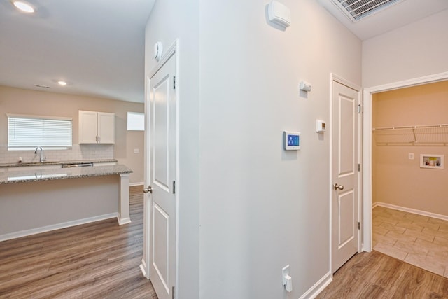 hallway with recessed lighting, visible vents, a sink, light wood-type flooring, and baseboards