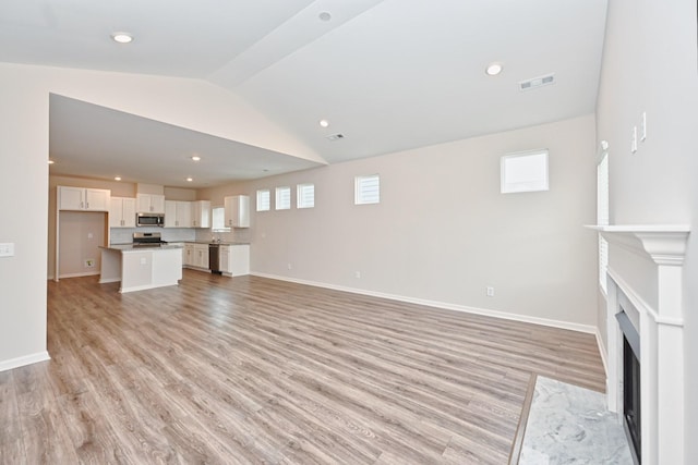 unfurnished living room featuring a fireplace with flush hearth, light wood-type flooring, visible vents, and vaulted ceiling