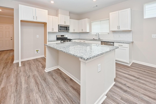 kitchen featuring white cabinets, a kitchen island, stainless steel appliances, light wood-type flooring, and a sink