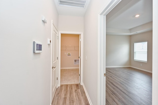 corridor with light wood-type flooring, visible vents, and baseboards