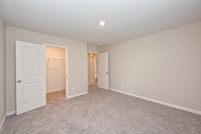 unfurnished bedroom with carpet, a spacious closet, baseboards, and a closet