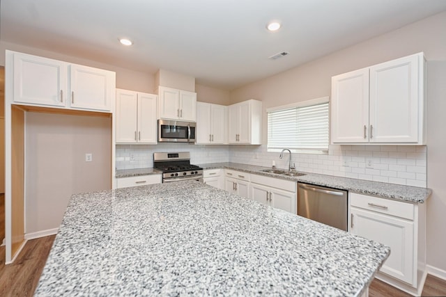 kitchen featuring appliances with stainless steel finishes, a sink, white cabinetry, and light stone countertops