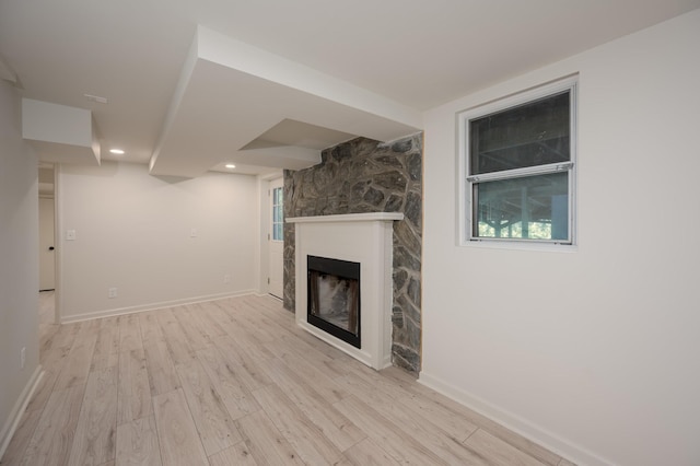 unfurnished living room with a stone fireplace, recessed lighting, light wood-style flooring, and baseboards