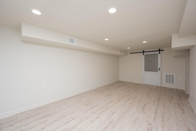 empty room featuring a barn door, light wood-style flooring, visible vents, and recessed lighting