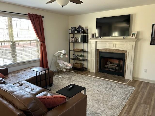 living room featuring a ceiling fan, a fireplace, baseboards, and wood finished floors