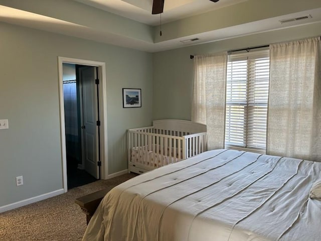 carpeted bedroom featuring visible vents, baseboards, and a raised ceiling