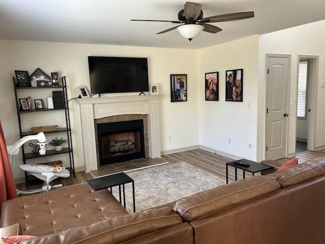 living area featuring a tiled fireplace, wood finished floors, a ceiling fan, and baseboards