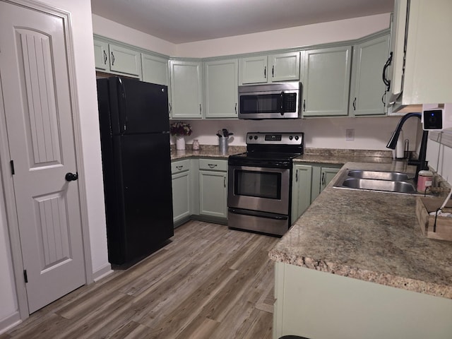 kitchen with appliances with stainless steel finishes, a sink, and light wood-style flooring