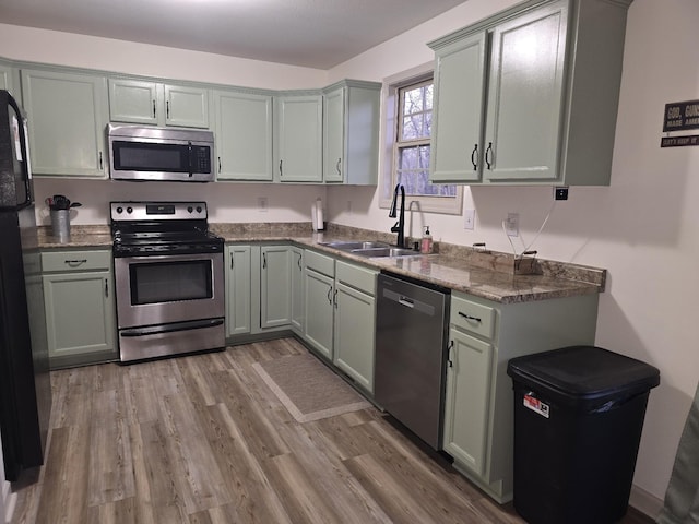 kitchen featuring wood finished floors, appliances with stainless steel finishes, dark stone counters, and a sink