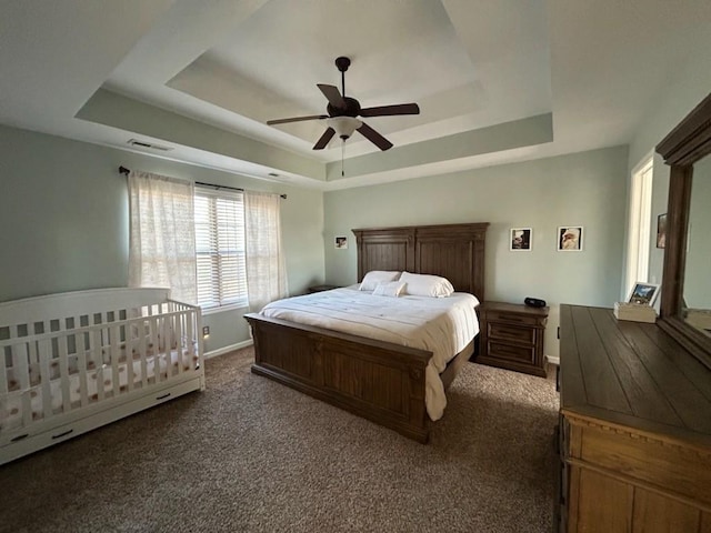 bedroom featuring baseboards, visible vents, a tray ceiling, and dark carpet