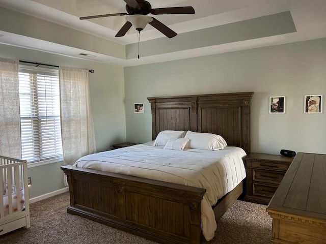 bedroom with ceiling fan, visible vents, baseboards, dark colored carpet, and a tray ceiling