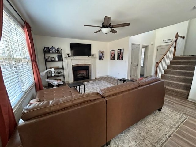 living area with a ceiling fan, wood finished floors, a fireplace, and stairs