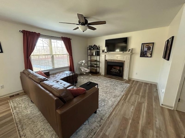 living area featuring baseboards, a ceiling fan, wood finished floors, and a tile fireplace