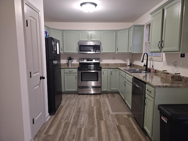 kitchen featuring stainless steel appliances, dark stone counters, a sink, and light wood-style flooring