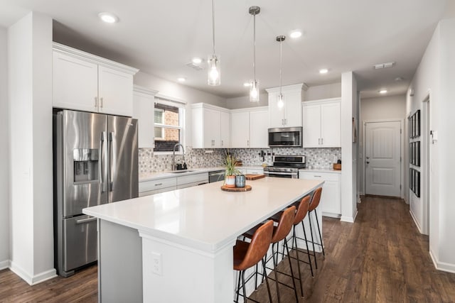 kitchen with decorative backsplash, appliances with stainless steel finishes, white cabinetry, a sink, and a kitchen island