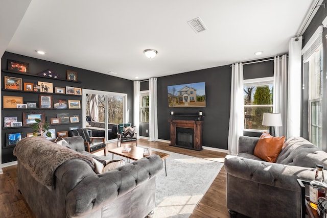 living area featuring recessed lighting, wood finished floors, visible vents, baseboards, and a glass covered fireplace